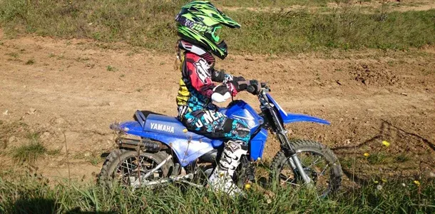 Kind auf einer blauen Kindermotocross-Maschine auf der Strecke