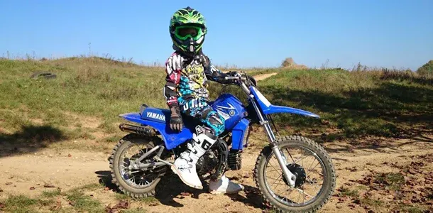 Kind mit grünem Helm auf einer blauen Kindermotocross-Maschine
